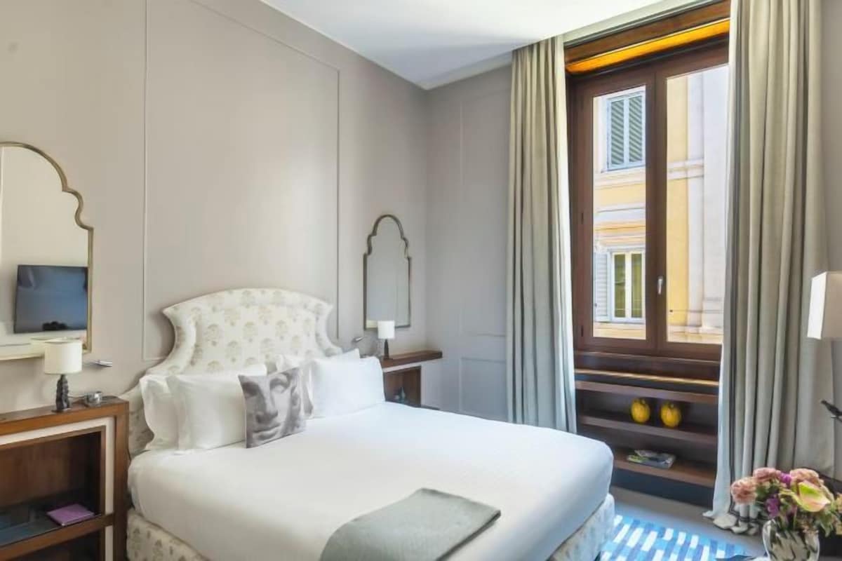 Quarto de hotel com cama, mesa de cabeceira, espelho, janela com cortinas e vista para o exterior.