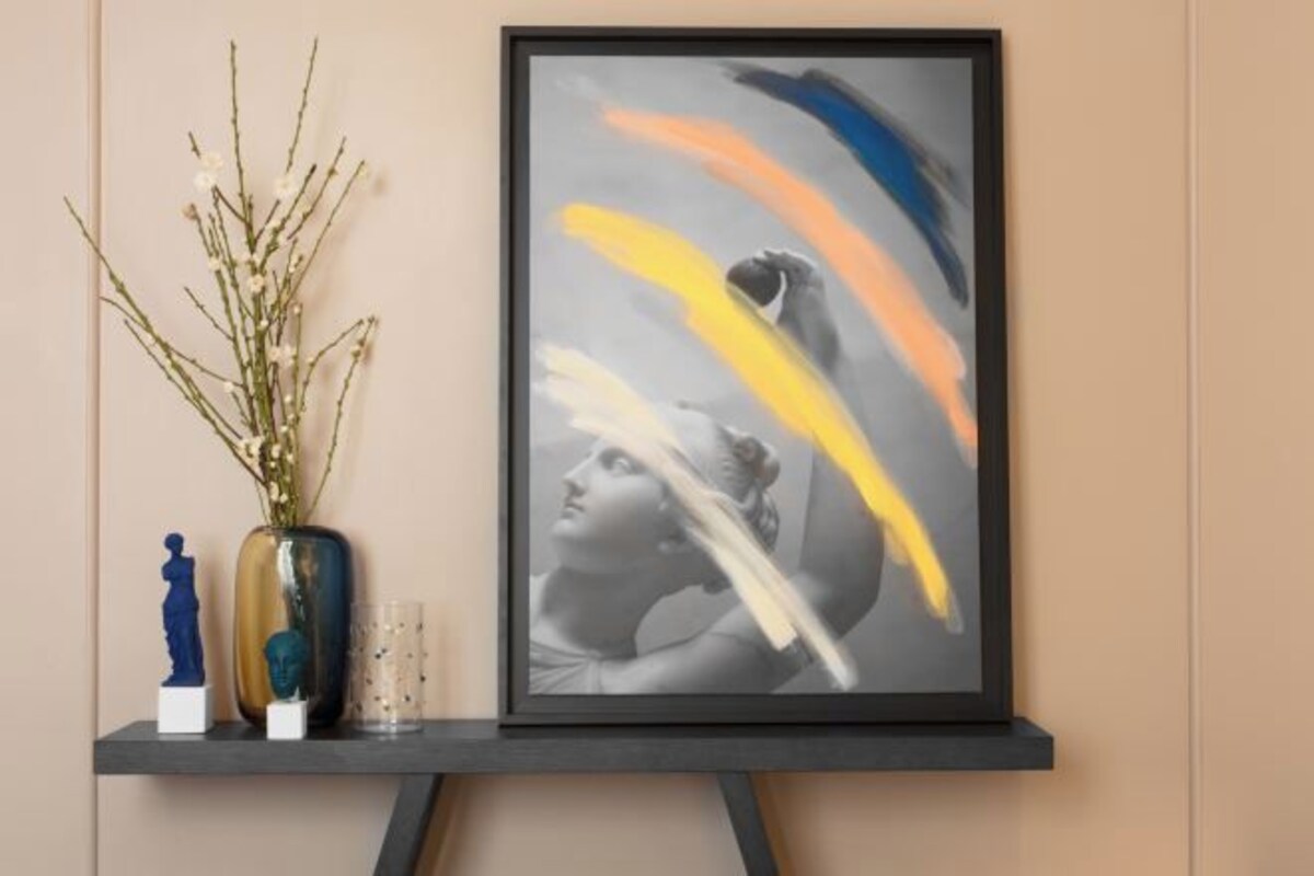 A framed artwork on a wall, a vase with branches, and two small statues on a shelf.