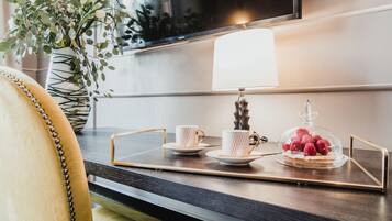 Ein modernes Hotelzimmer mit einem Holztisch, einem Glastisch, einer Lampe, einer Vase mit Grünpflanzen und einem an der Wand befestigten Fernseher.