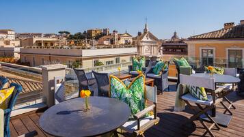 A rooftop terrace with outdoor seating, a view of the cityscape, and a small church in the background.