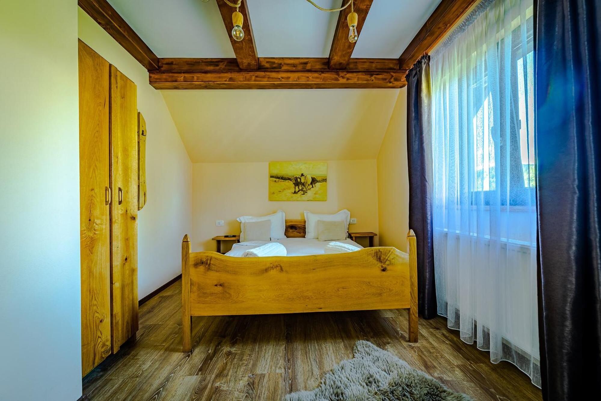 A bedroom with a wooden bed, a painting on the wall, and a window with curtains.
