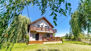 A two-story house with a balcony, surrounded by greenery and a well-maintained lawn. - Casa Nitu (Întorsura Buzaului)