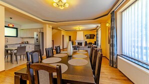 A modern dining area with a long table, chairs, and a chandelier. - Casa Nitu (Întorsura Buzaului)