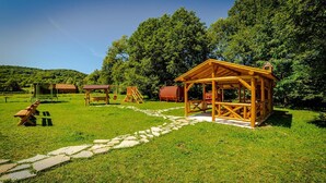 A rustic wooden cabin with a stone pathway leading to it, surrounded by lush greenery and trees. - Casa Nitu (Întorsura Buzaului)