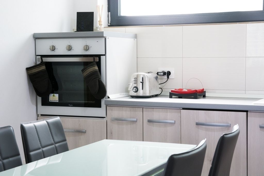 A compact kitchen with a built-in oven, a toaster, and a small refrigerator. There is a dining table with chairs and a window above the sink.