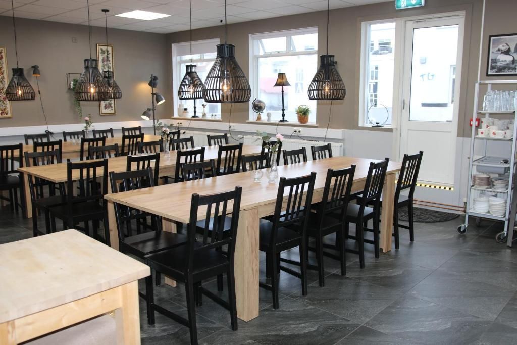 A dining area with multiple tables and chairs, pendant lighting, and a view of the street through large windows.