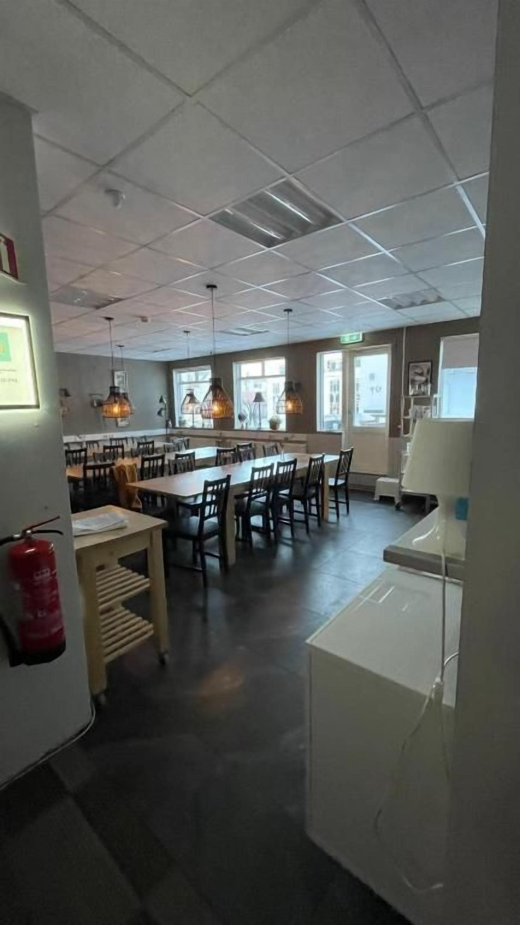 Un comedor amplio con varias mesas y sillas, un extintor en la pared y un electrodoméstico blanco al frente.
