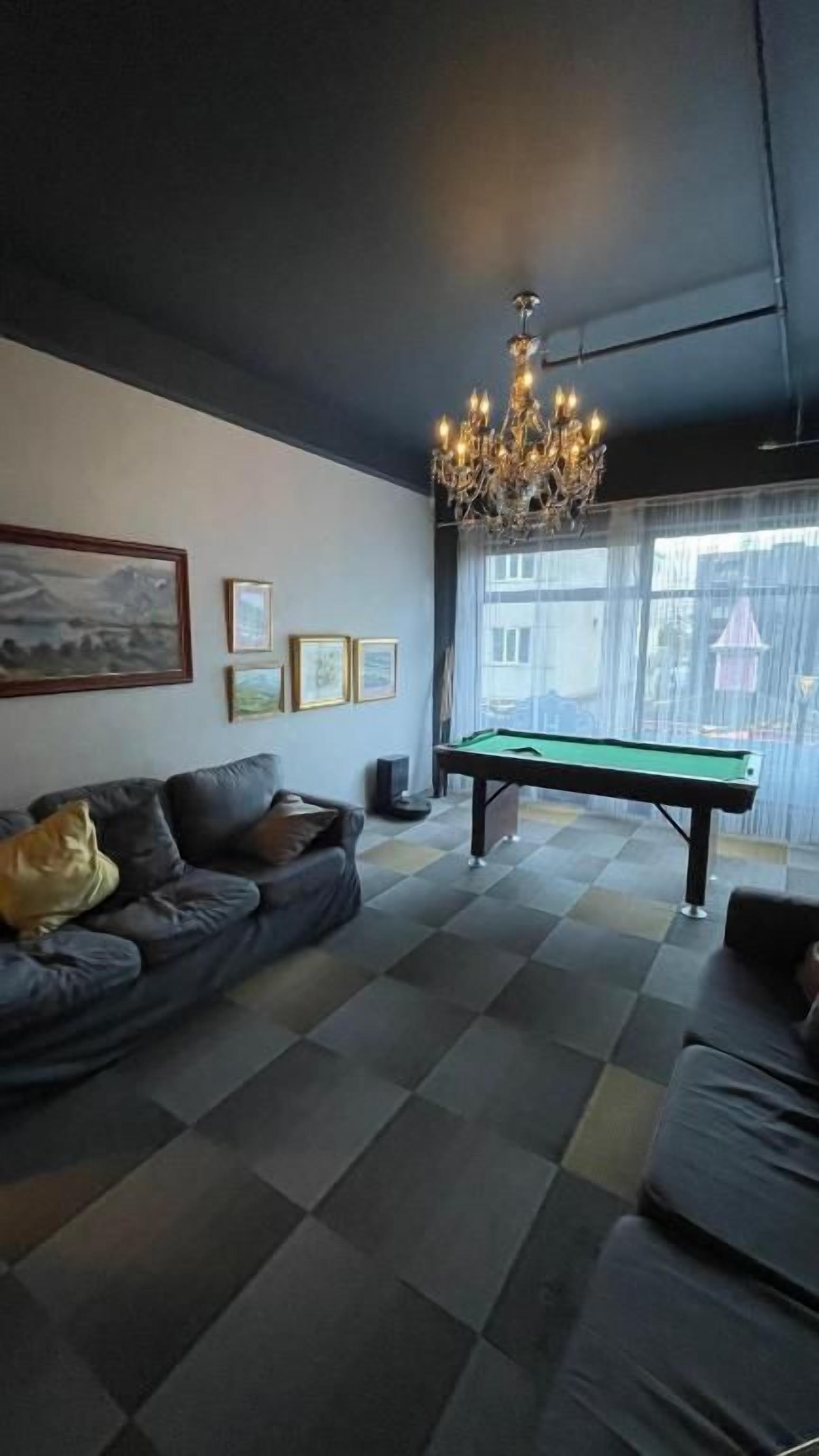 Una habitación con mesa de billar, sofá, candelabro y cuadros en la pared.