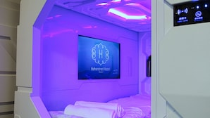 Una habitación con una cama, una pantalla de televisión mostrando 'Hafnarstræti Hostel Akershus' y un panel de control con un símbolo de Wi-Fi.