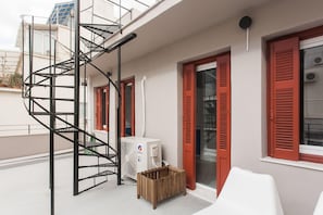 Un immeuble d’habitation doté d’un escalier en colimaçon, de volets rouges et d’un climatiseur blanc.