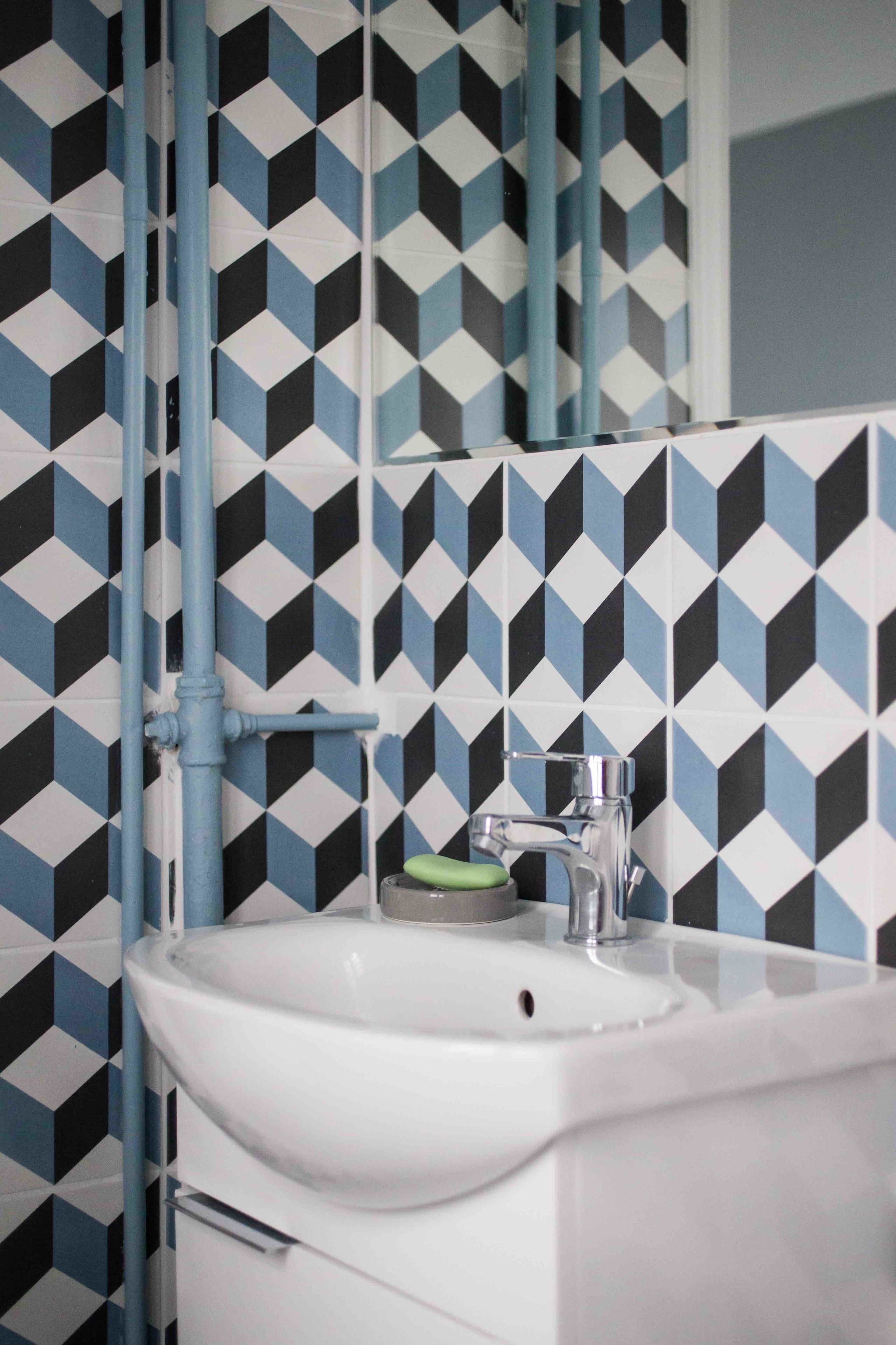 A bathroom with a geometric patterned tile wall, a white sink, and a mirror above it.