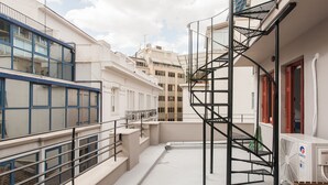 Una terraza en la azotea con una escalera espiral, barandillas y una unidad de aire acondicionado blanca.