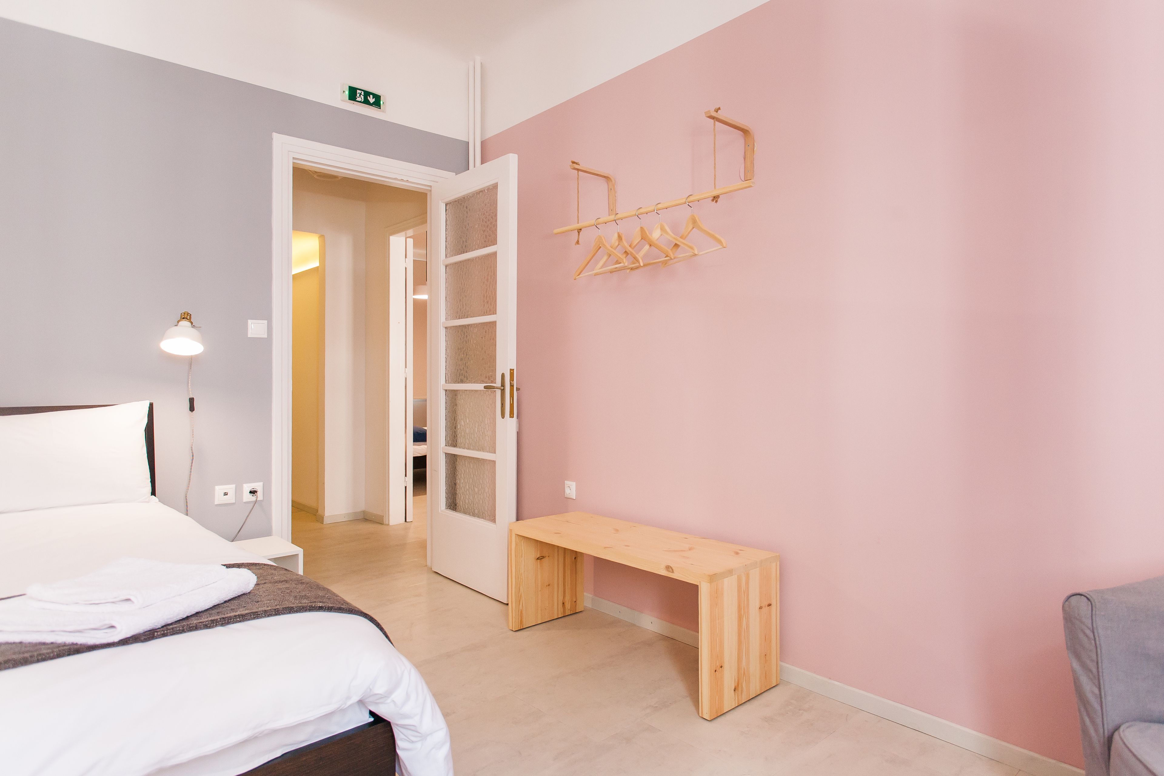 A hotel room with a bed, a bench, a wooden hanger rack, and a door leading to a bathroom.