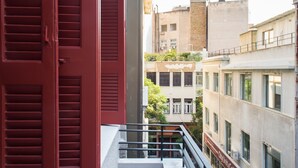 Un balcón con contraventanas rojas, barandilla blanca y vistas de edificios cercanos.