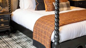 A four-poster bed with a black frame, white bedding, and a brown throw blanket. There are two framed equestrian paintings on the wall above the bed.