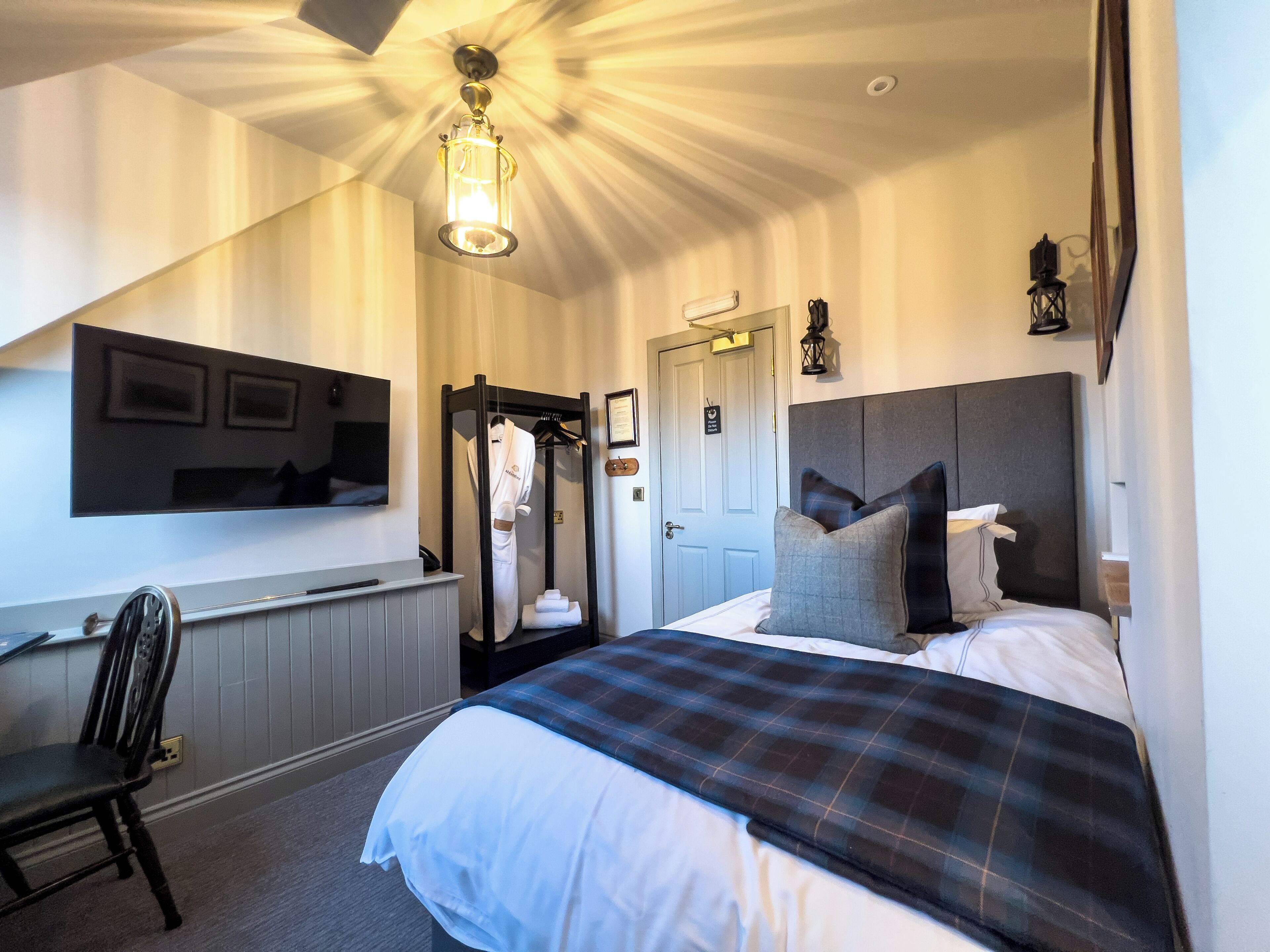 A hotel room with a bed, a desk, a chair, a wardrobe, and a mirror.