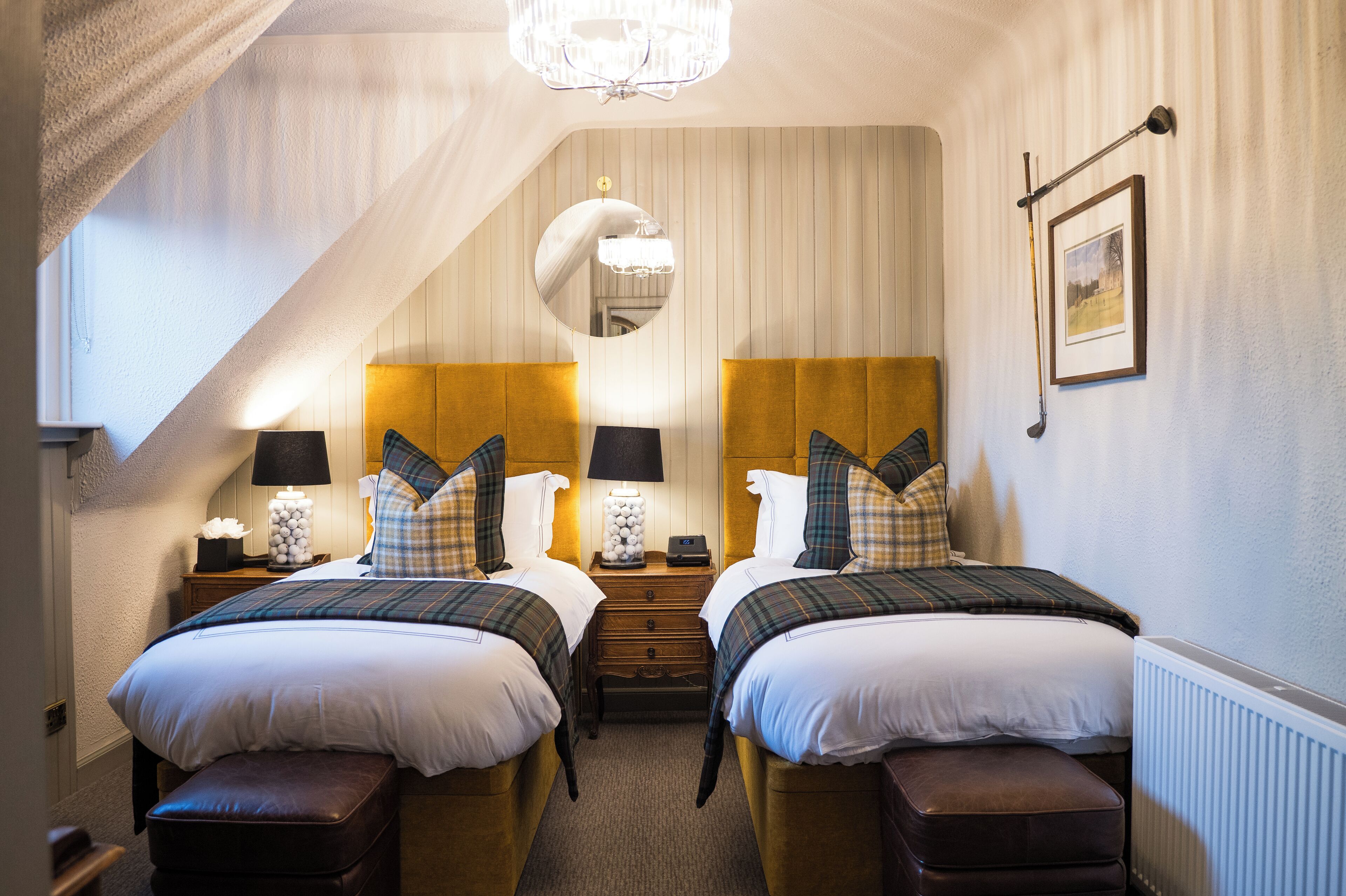A bedroom with two beds, a chandelier, a mirror, and a framed picture on the wall.
