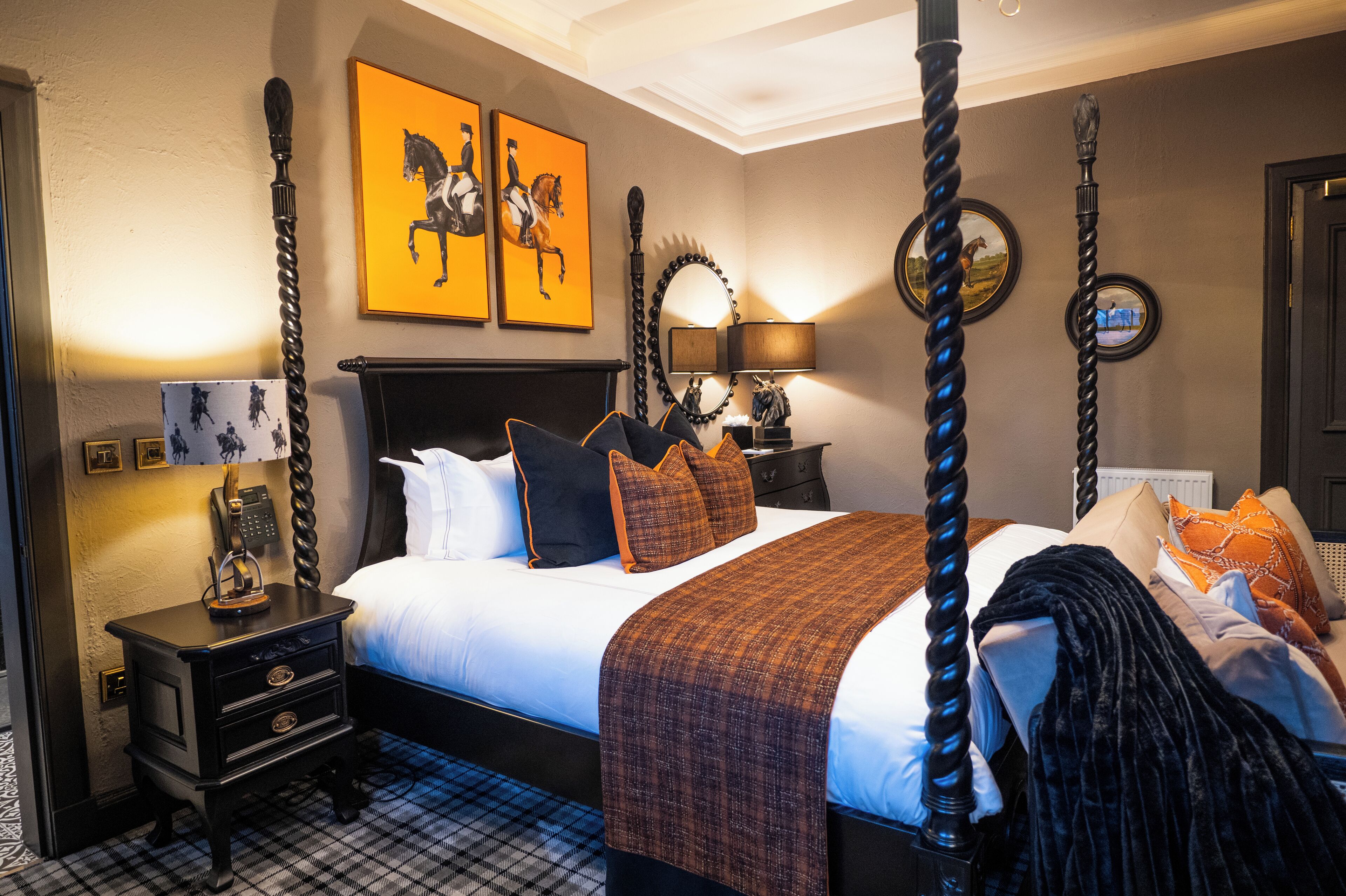 A four-poster bed with a dark headboard, a bedside table with a telephone, and two wall-mounted lamps.