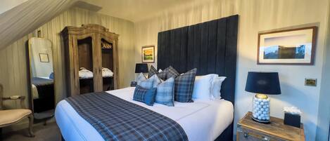 Een hotelkamer met een groot bed, een houten garderobe, een bureau met lamp en een kroonluchter.