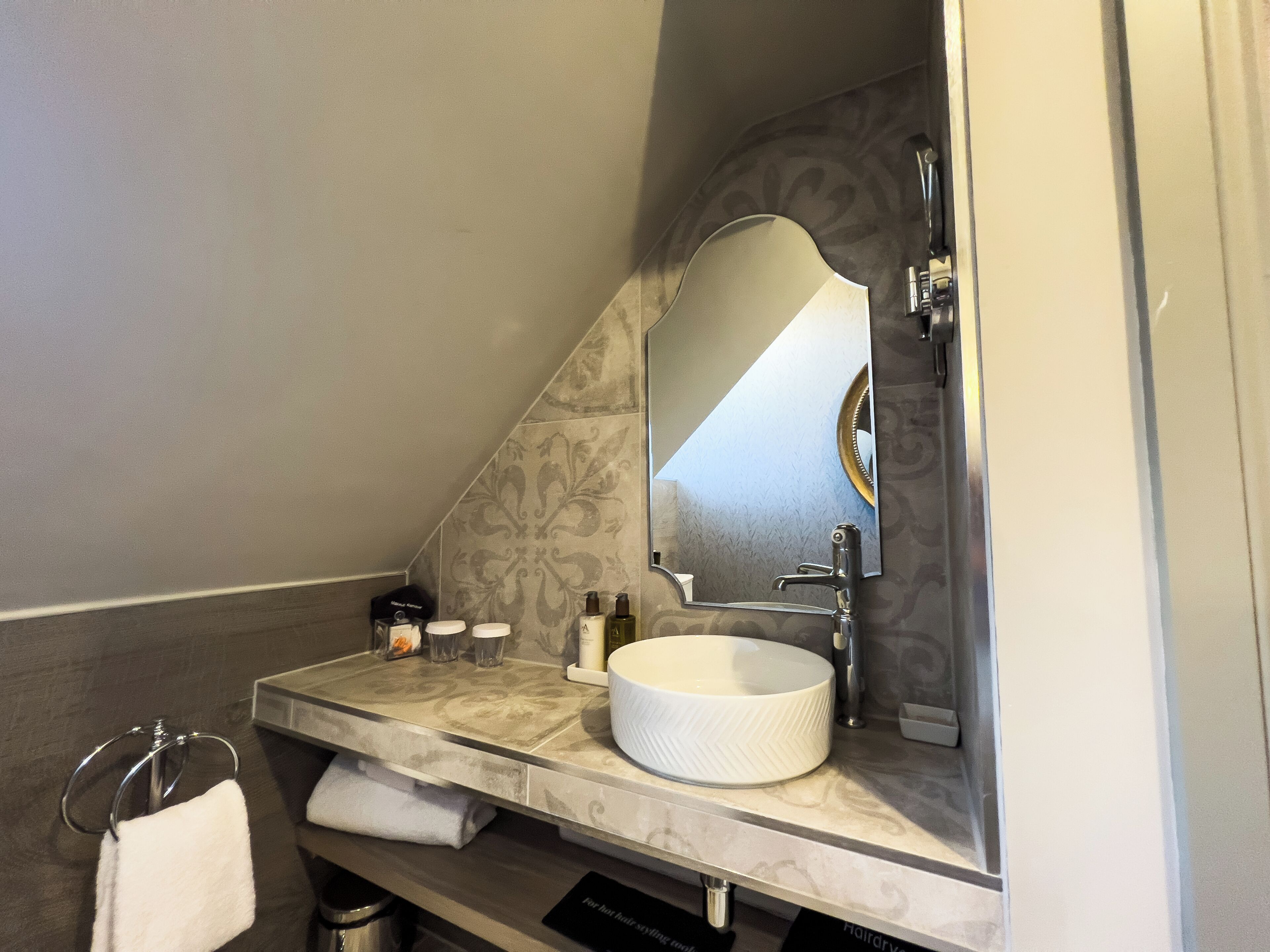 A bathroom with a marble vanity, a white sink, a large mirror, and a towel rack.
