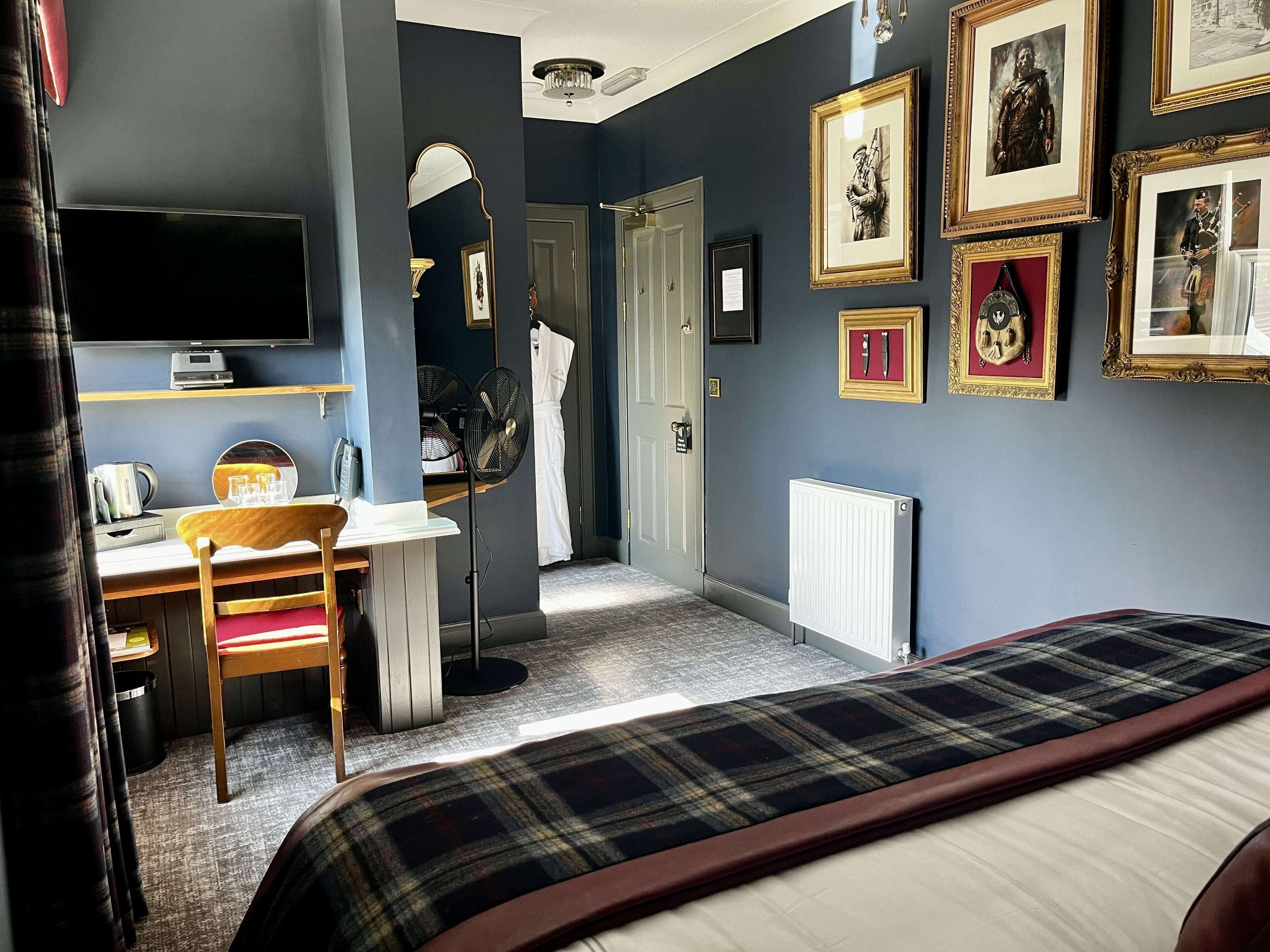 Ein Schlafzimmer mit einem Bett, einem Schreibtisch, einem Stuhl, einem Spiegel und einer Wand mit gerahmten Bildern.