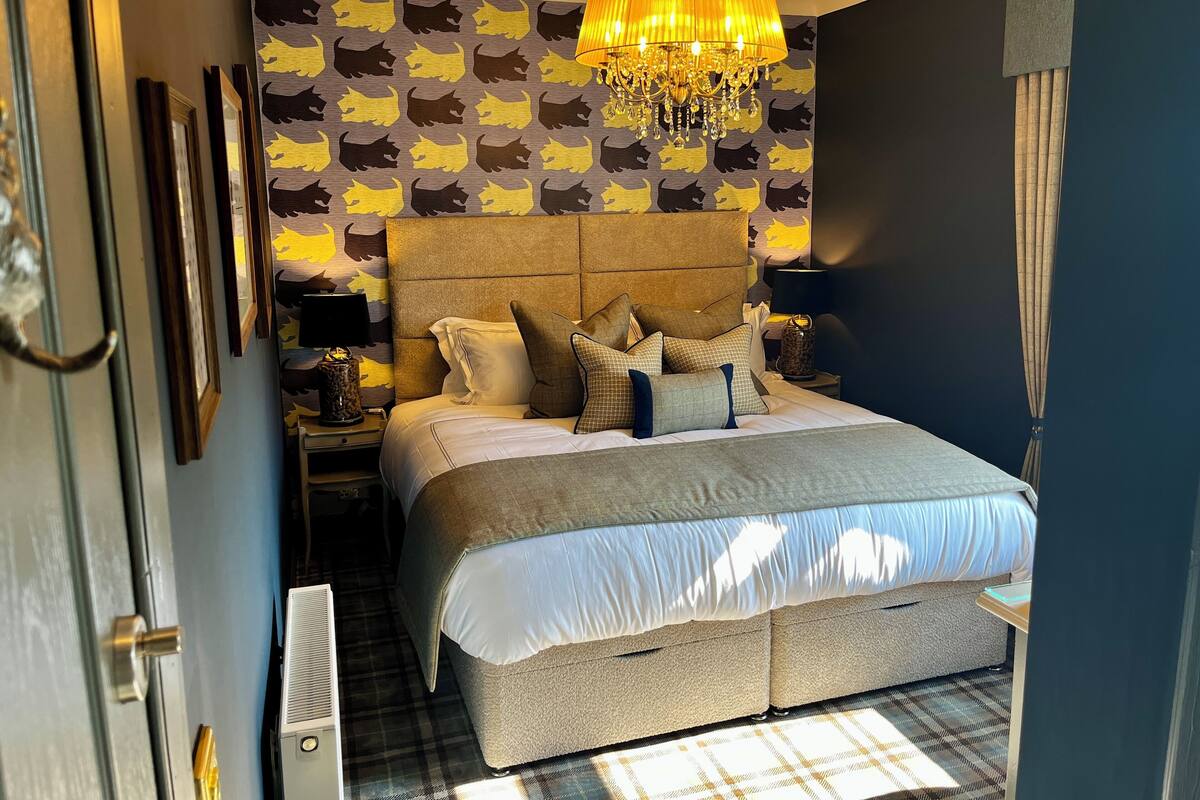A bedroom with a large bed, a chandelier, and a patterned wallpaper.