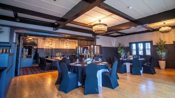 Un comedor amplio con techos altos y candelabros, suelo de madera y sillas tapizadas en azul oscuro.