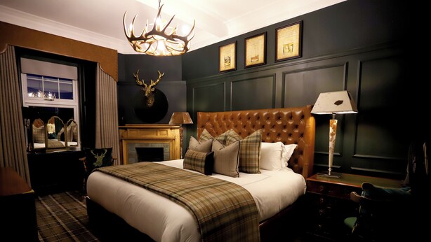 A hotel room with a large bed, a fireplace, a mounted deer head, and a chandelier. - Abbotsford Hotel (Ayr)