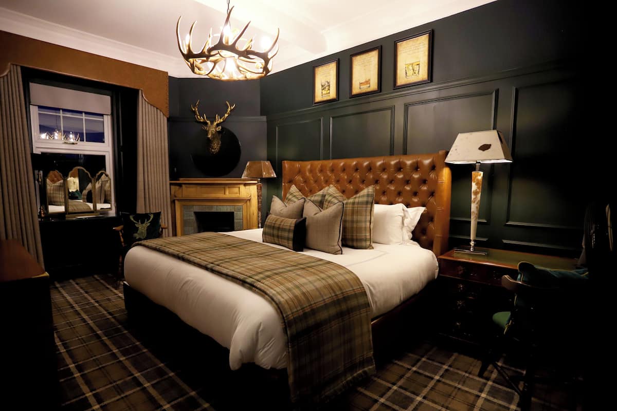 A hotel room with a large bed, a fireplace, a mounted deer head, and a chandelier.