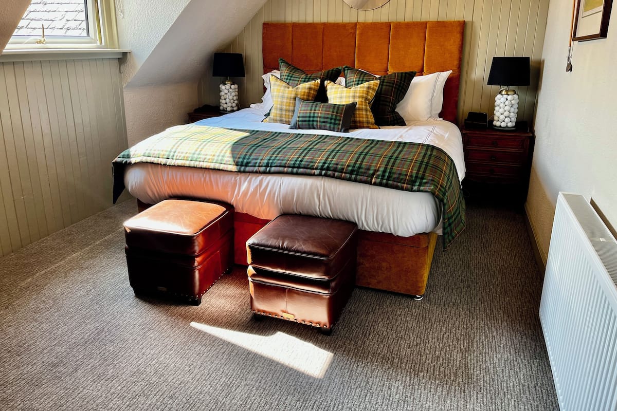A bedroom with a large bed, two nightstands, a wooden headboard, and a window.