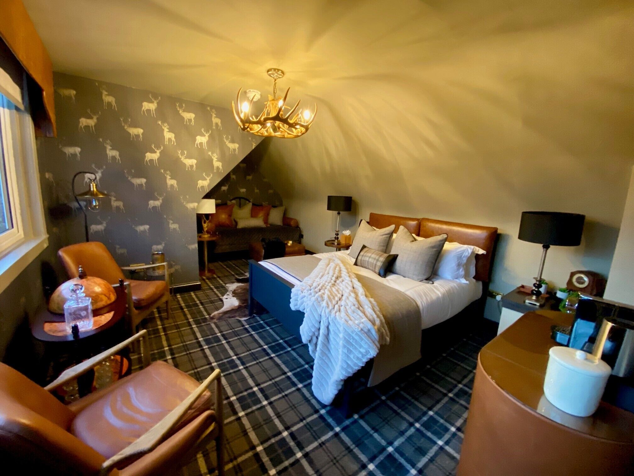 A hotel room with a bed, a chair, a nightstand, a lamp, and a chandelier.