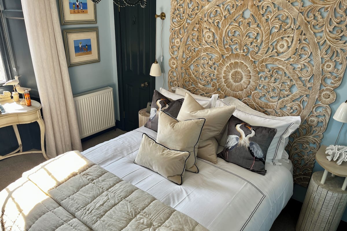 A bedroom with a large bed, a decorative headboard, a bedside table with a lamp, and framed pictures on the wall.