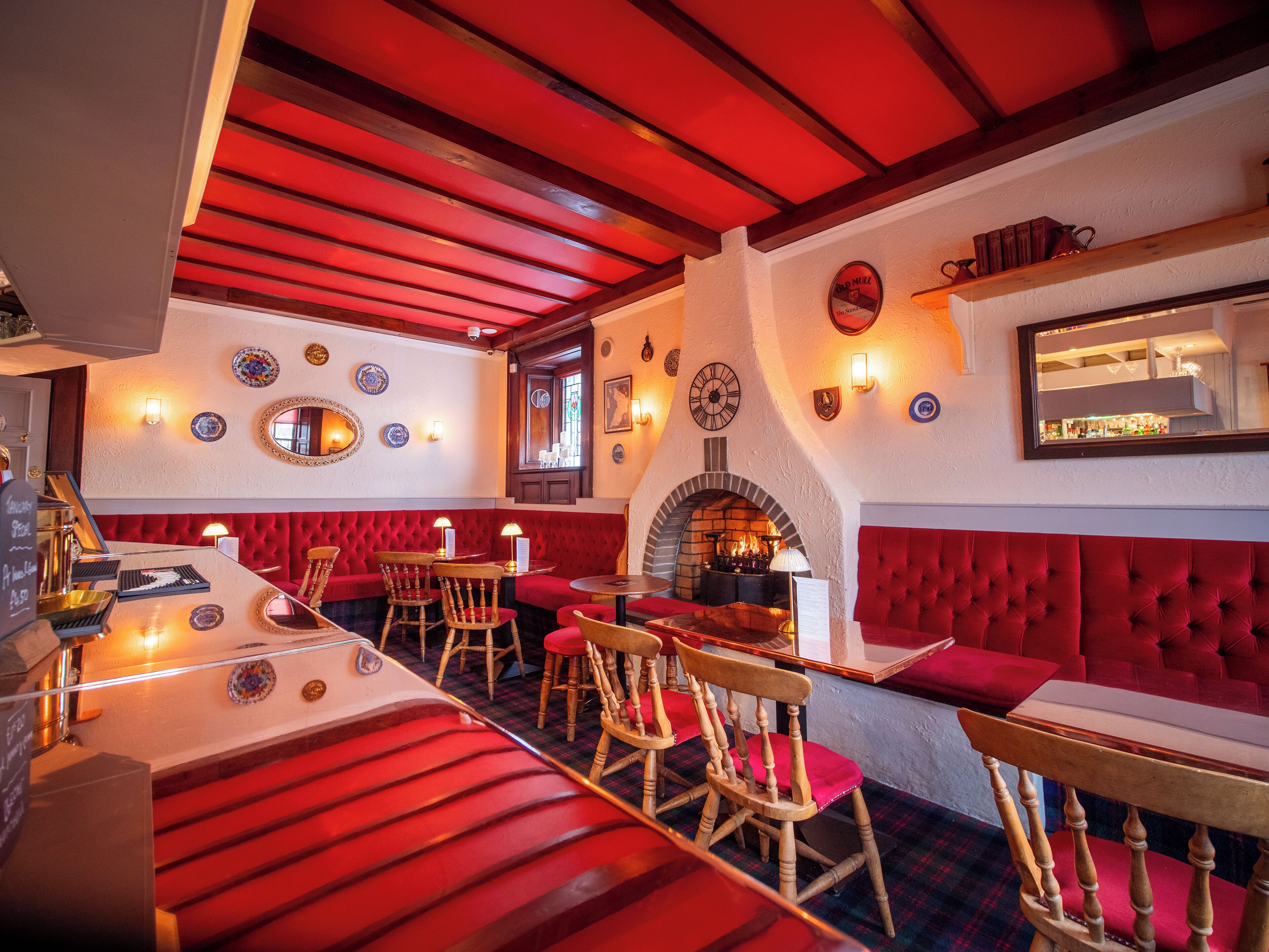 A cozy restaurant interior with red upholstered seating, a brick fireplace, and a variety of wall decorations including plates and a clock.
