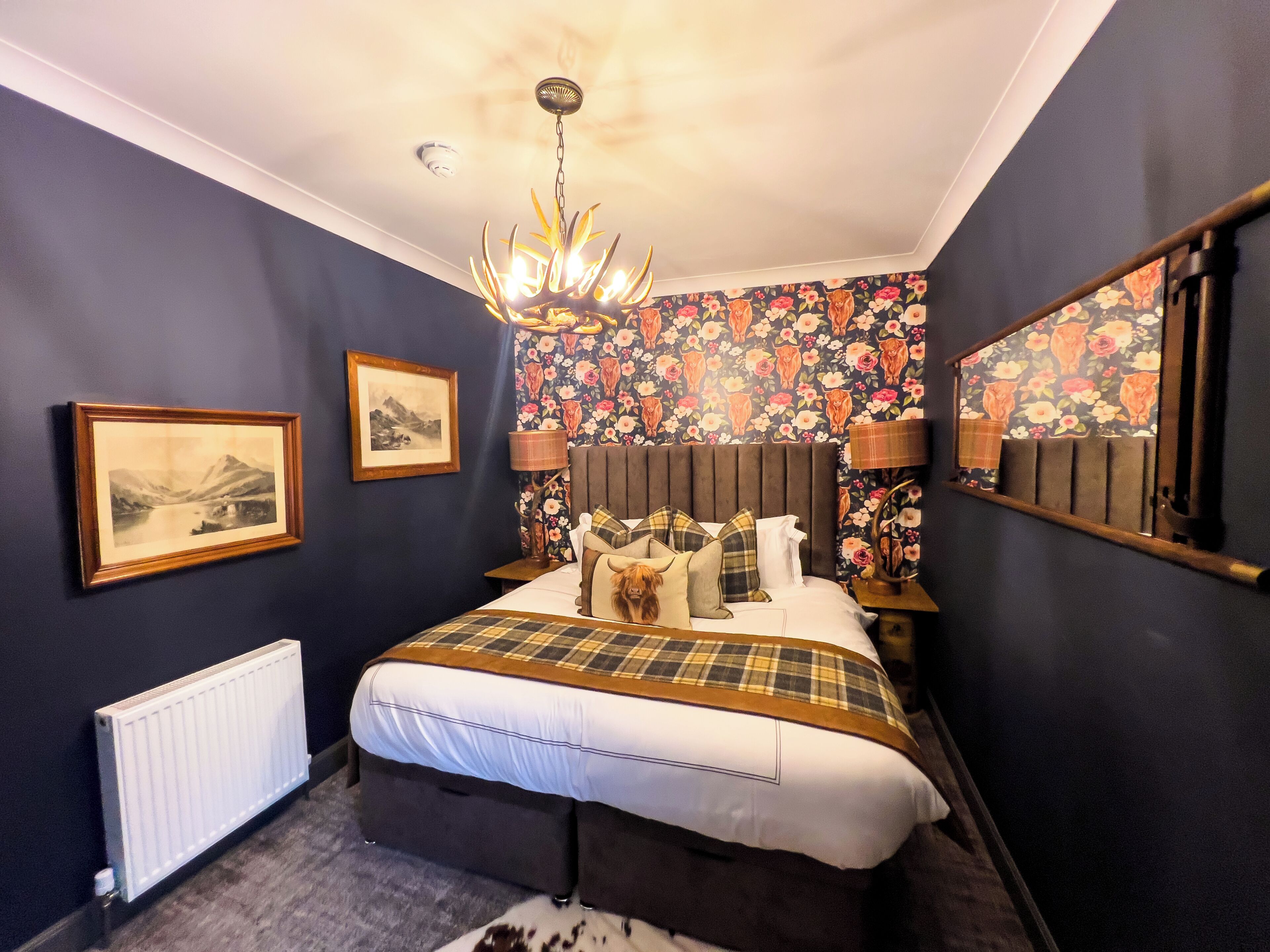 Une chambre à coucher avec un lit, un lustre, un radiateur et un papier peint à motifs floraux.