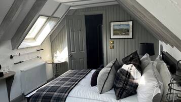Un dormitorio con techo inclinado, una cama con ropa de cama escocesa, una mesita de noche con lámpara y un cuadro en la pared.