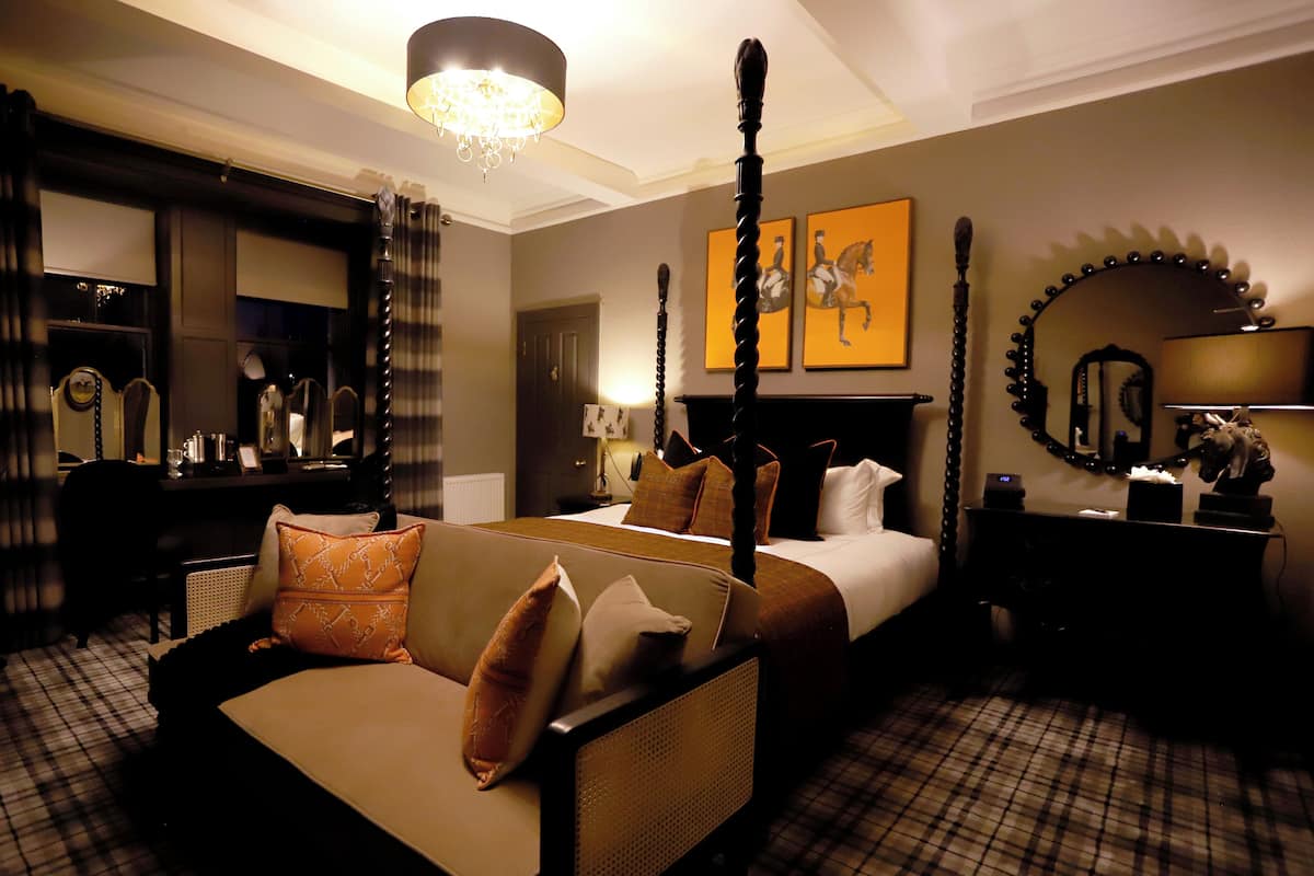 A four-poster bed with a canopy, a sofa with patterned cushions, a mirror with lights, and a checkered floor.
