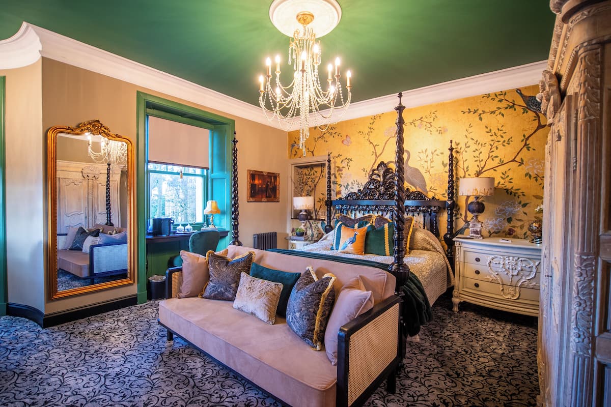 A bedroom with a four-poster bed, a sofa, a mirror, and a chandelier.