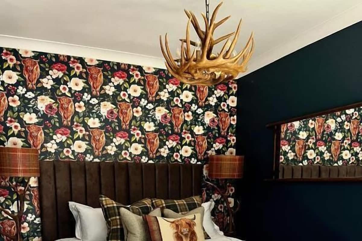 A bedroom with a large bed, floral wallpaper, a wooden headboard, and a cowhide rug.