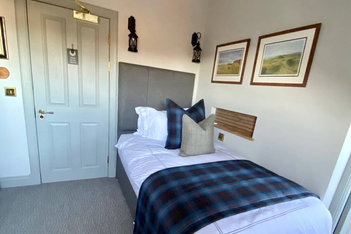 A bedroom with a bed, a headboard, a door, and two framed pictures on the wall.