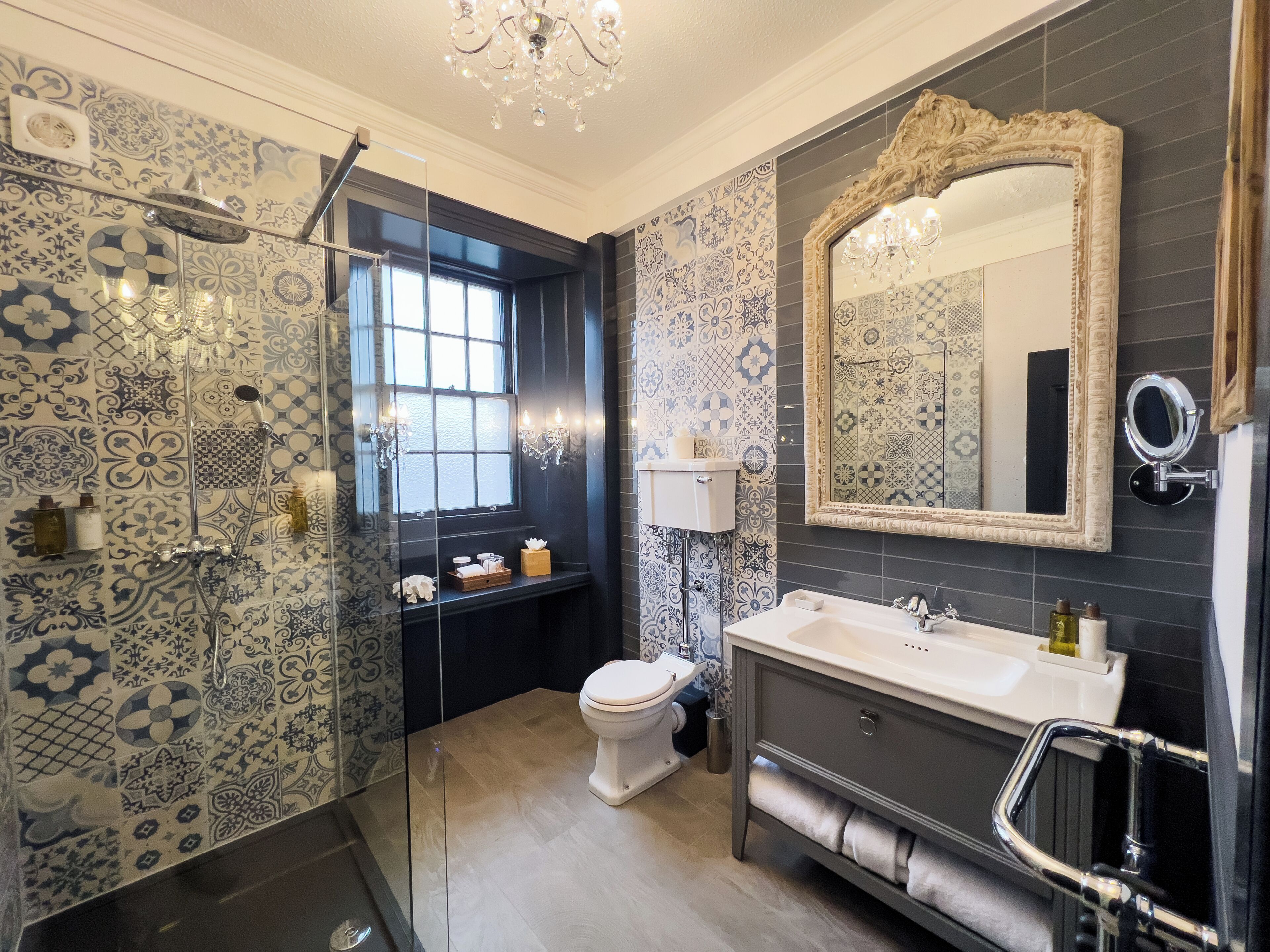 A bathroom with patterned tiles, a shower, a toilet, a sink, and a mirror.