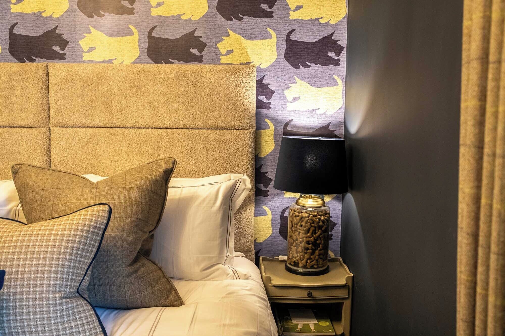 A hotel room with a tufted headboard, a bedside lamp, and a patterned wall.