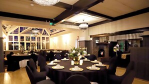 A dining area with round tables set for a meal, featuring a chandelier and a brick fireplace. - Abbotsford Hotel (Ayr)