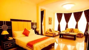A hotel room with a large bed, a bedside table with a lamp, a chair, a sofa, and a small table. - Star Hotel (Bujumbura)