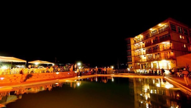 A nighttime view of a waterfront area with a building featuring multiple balconies and a pool reflecting the lights. - Star Hotel (Bujumbura)