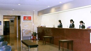 Zona de recepción con mostrador, un reloj y área de estar con sillas y un banco.