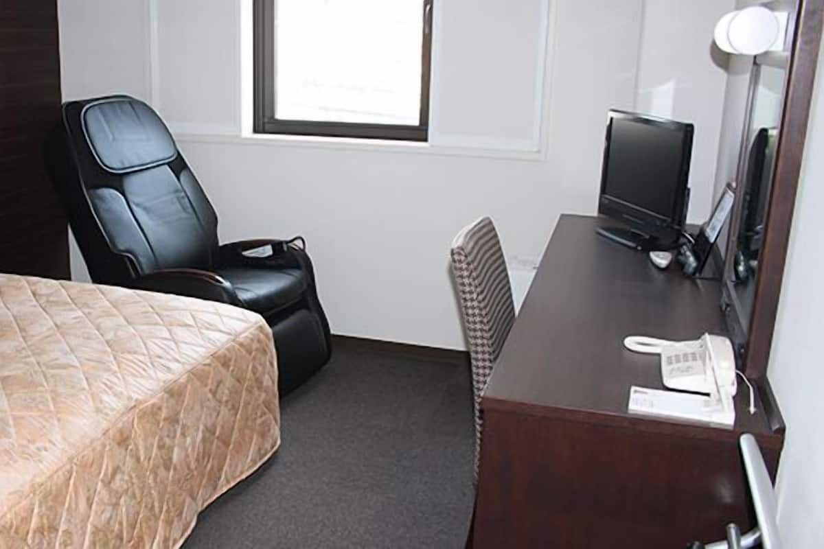 Ein Hotelzimmer mit einem Bett, einem Schreibtisch mit Computer, einem Stuhl und einem Fenster.