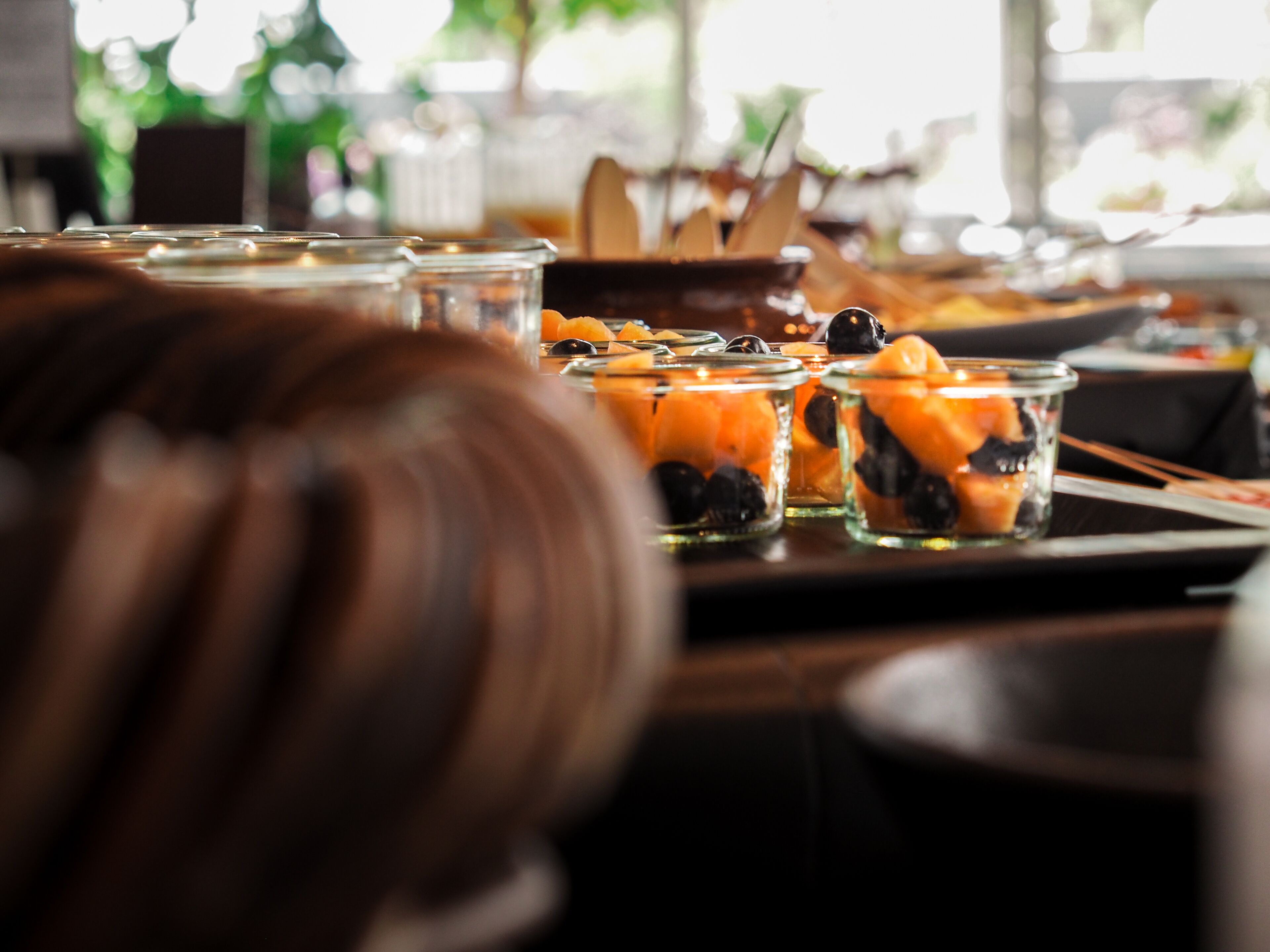Una mesa de buffet con diversos alimentos, como frutas y verduras, en recipientes de vidrio transparente.