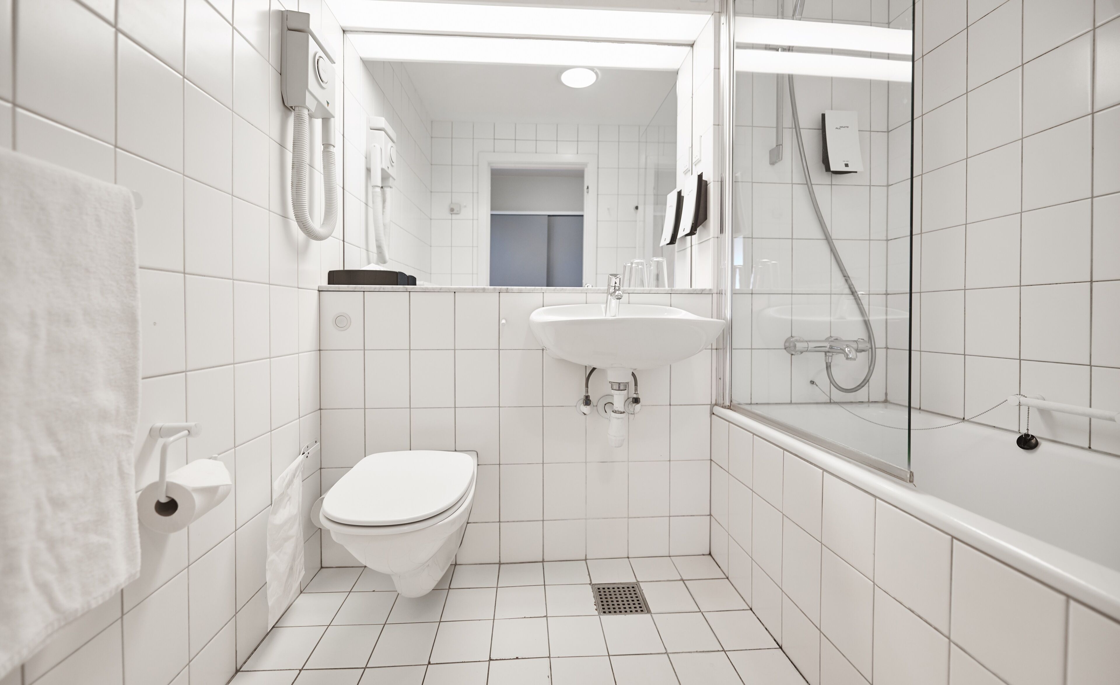 A small, white bathroom with a toilet, sink, and shower.
