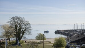 A marina with boats docked, a grassy area with trees, and a clear view of the water. - Hotel Marina (Vedbaek)
