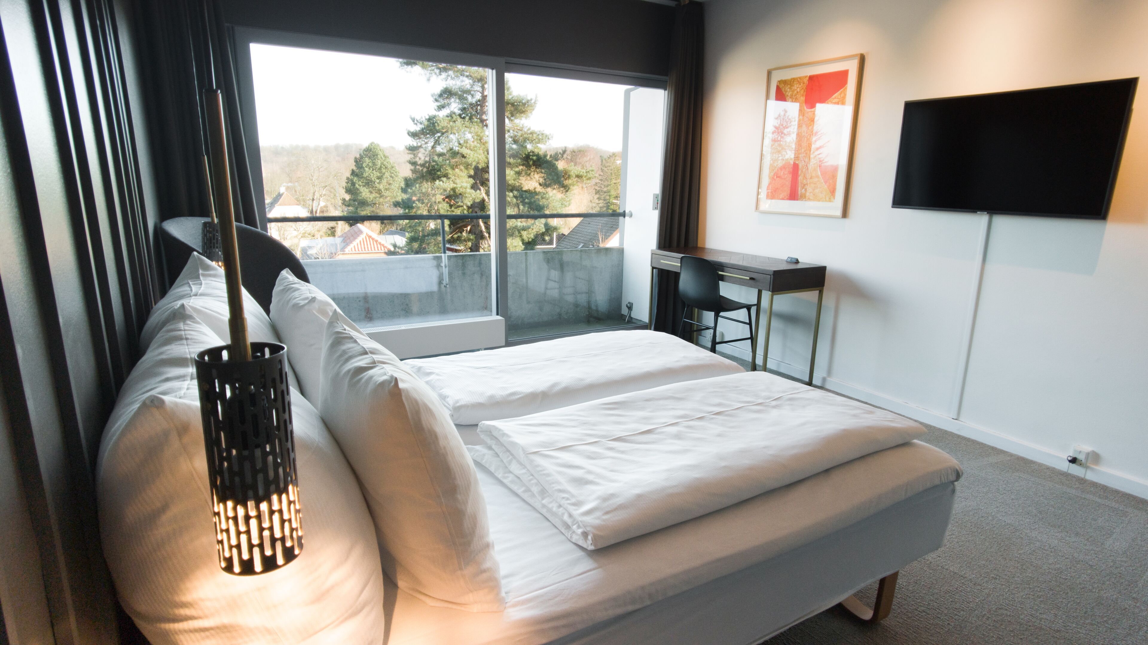 A modern bedroom with a large bed, a desk, and a TV.